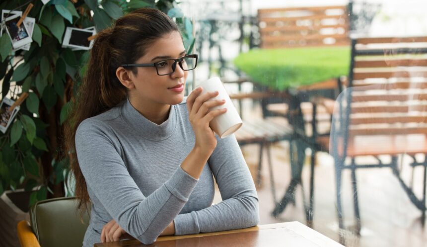 Intelligent young businesswoman having coffee break in cafe. Calm beautiful girl drinking tea and looking out window dreaming of success or love. Coffee shop concept